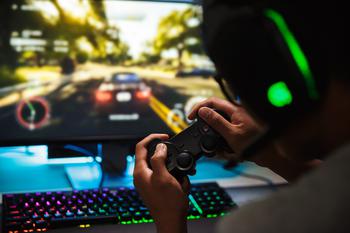 Teenage gamer wearing headphones and playing video games on computer in dark room. 