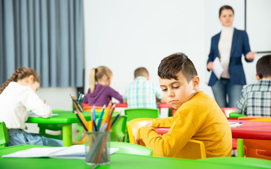 Tired schoolboy sitting in classroom looking away from teacher