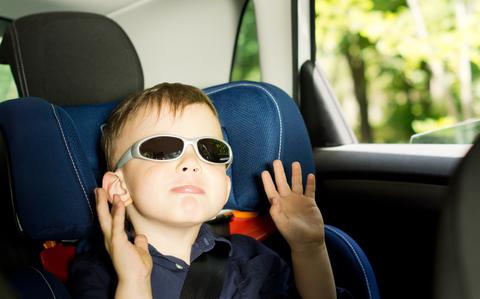 Photo Of Small boy raising arms while sitting in a child car-seat in the back of a car