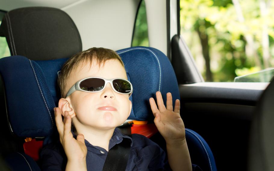 Small boy raising arms while sitting in a child car-seat in the back of a car