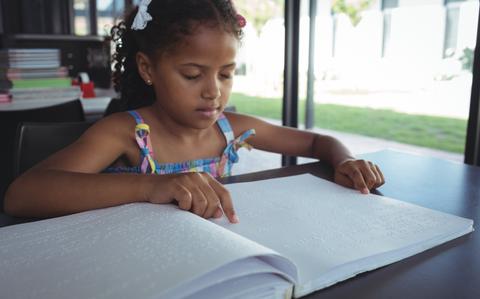 Photo Of Close up of girl reading braille at desk in library
