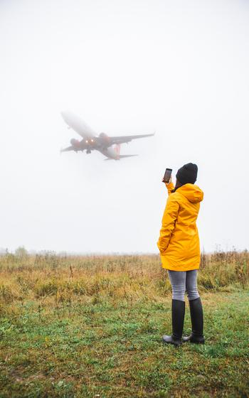 Woman in yellow raincoat taking picture of the landing plane copy space