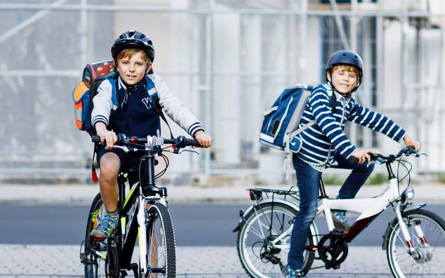 Two school kid boys in safety helmets riding with bike in the city with backpacks. 