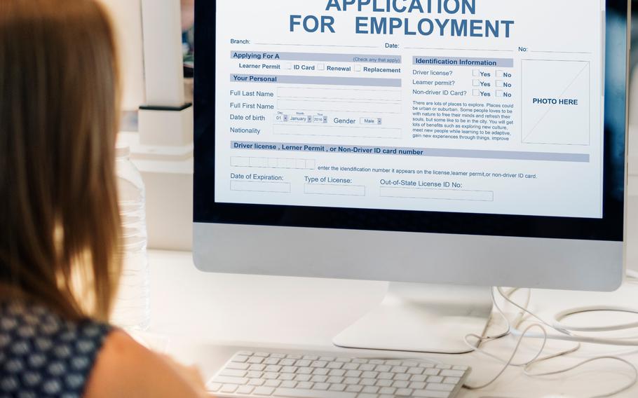 Point of view: From behind, women looking a computer screen. Orange highlighter and cell phone infront of computer keyboard. On computer screen it reads “Application for Employment” contains fill in the blank options.