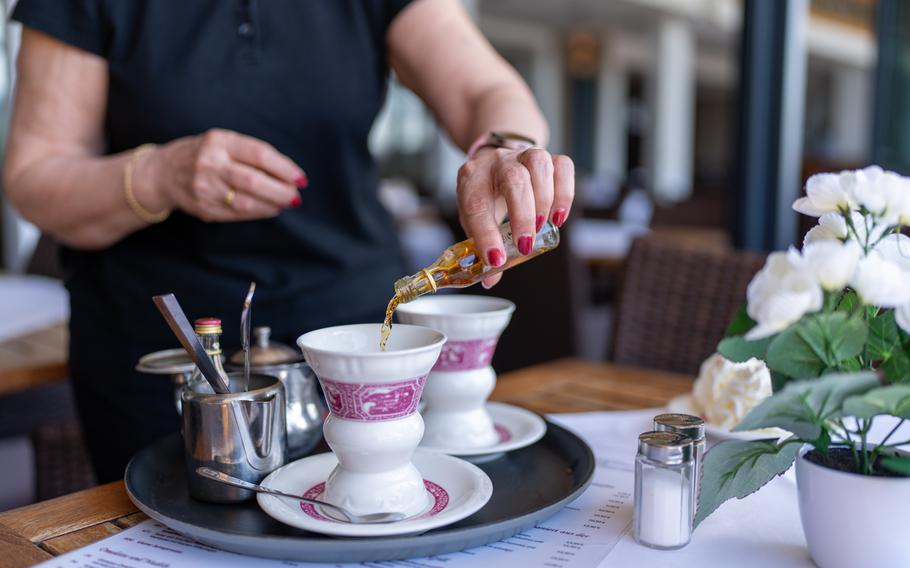 Waitress pouring flavored syrup into a traditional coffee cup at an outdoor cafe, adding a touch of sweetness.
