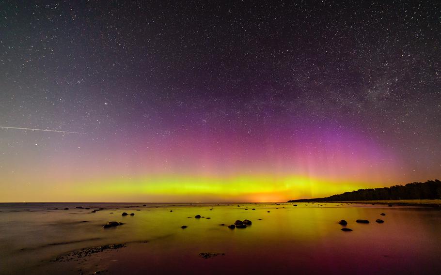 water on a beach reflecting rare, purple, red and nearly yellow ribbons of the northern lights in the night sky.