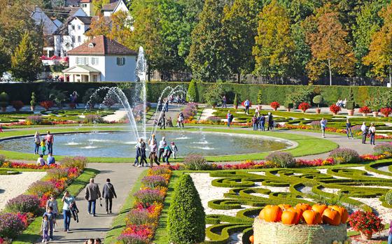 A colorful fall picture with a maze of gardens, a circular fountain, and pumpkins 