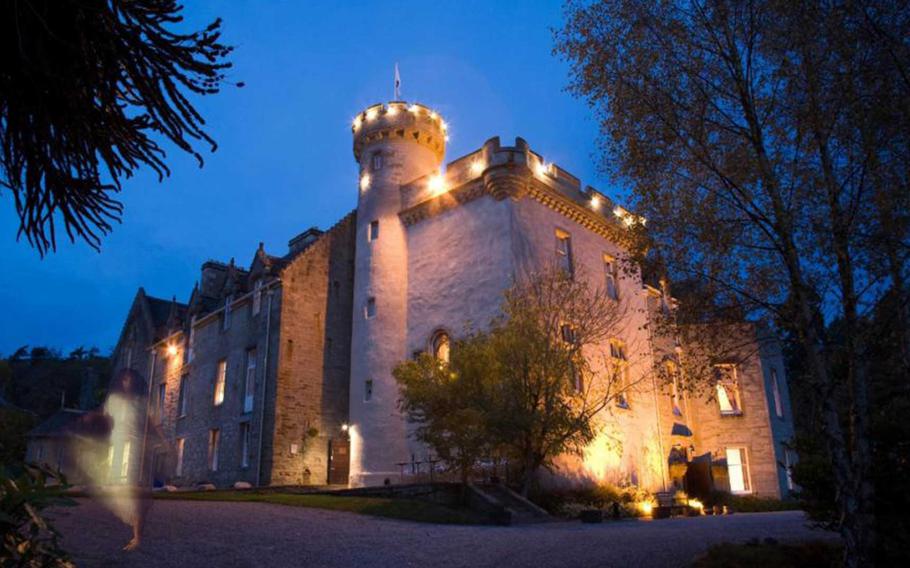 A nighttime image of Tulloch Castle, its stone walls lit warmly against the evening sky, with a faint apparition of a ghostly figure adding an eerie and mysterious atmosphere.