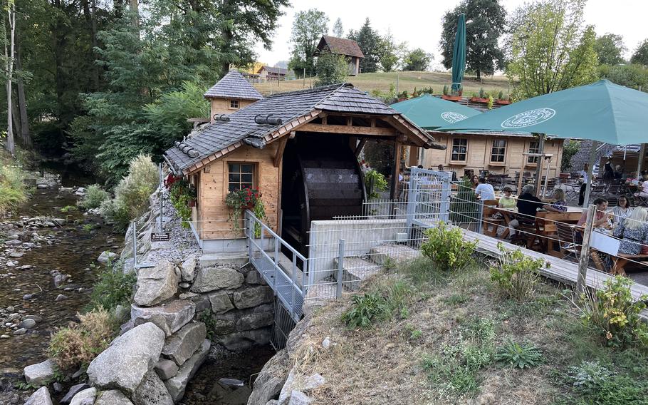 a cabin-style restaurant sites on rocks atop a river. people are outside enjoying meals under the shade of green umbrellas. 