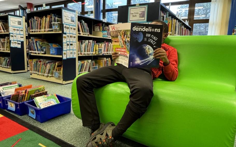 Second-grade student at Ramstein Elementary School library reading the Fall 2024 “Dandelions” magazine.