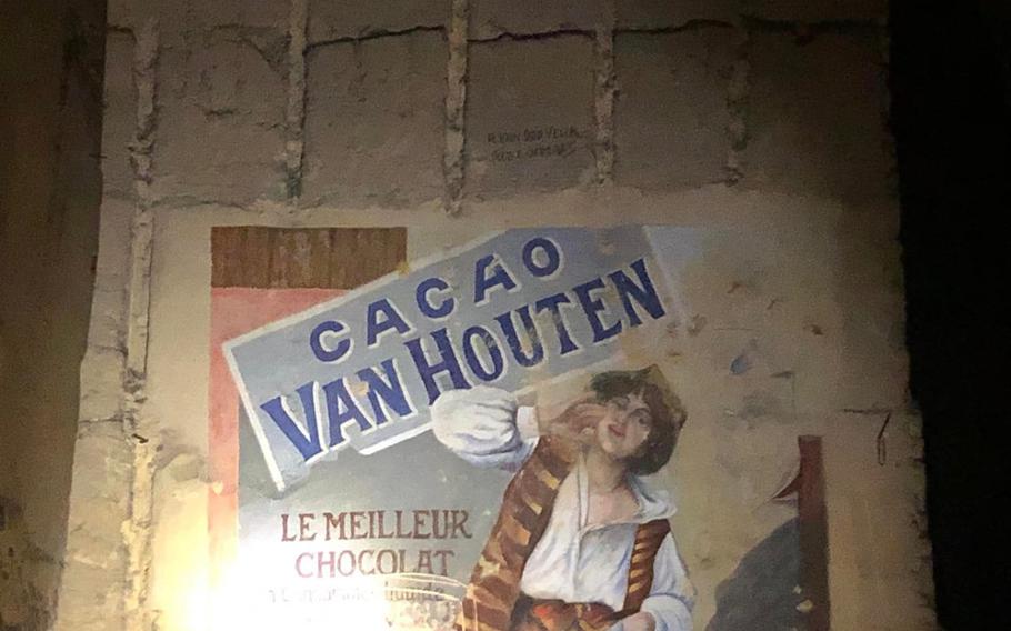 “Cacao Can Houten” ad inside of cave written in French featuring a paiting of a working class person.