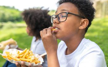 Child sitting on grass in park and eating fries on a sunny day