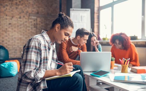 Group of four students getting together to study with a laptop, notebooks and pencils.