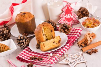 Panettone, traditional italian christmas cake with raisins on white plate surrounded by Christmas decorations.