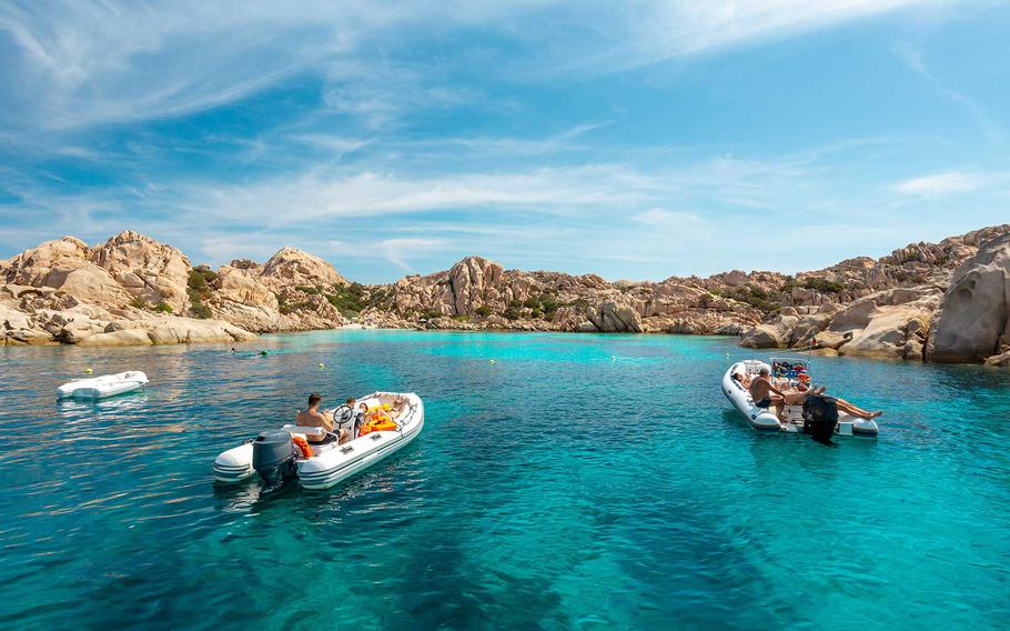 A stunning view of La Maddalena Archipelago National Park, showcasing its clear turquoise waters, rugged rock formations, and boats drifting leisurely under the Mediterranean sun.