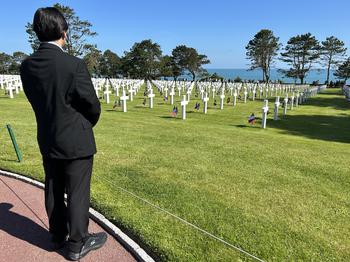 Author standing with back towards audience on the left side of the picture looking at the cemetery on a sunny day.