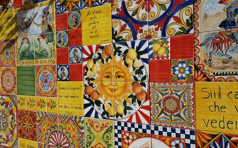 Photo Of Artistic tile wall featuring a sun, Italian words and flowery patterns