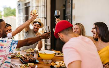 Group of friends toasting with wine while eating around a table.