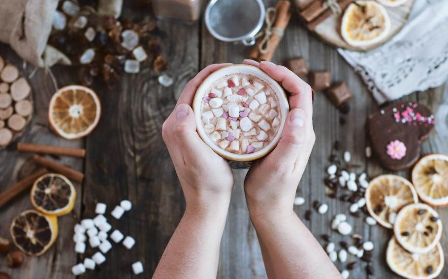 Hands holding hot cocoa wiht toppings around on the table