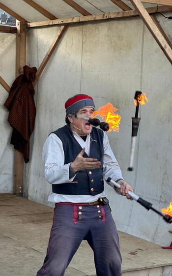 A performer throws three twirling batons lit with fire into the air 