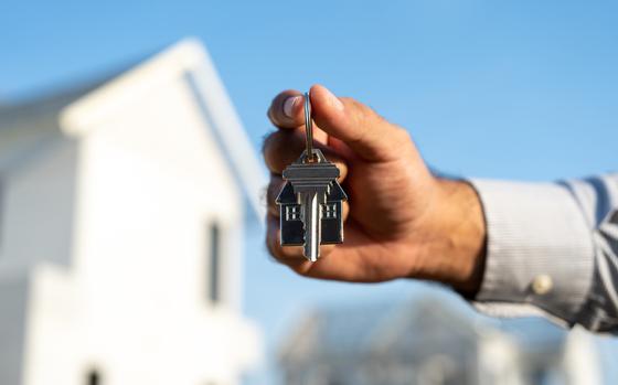 Close up male hand holding house key with sunlight. Real estate agent at construction site. New home purchase sales or rent. Choose Planning to buy property