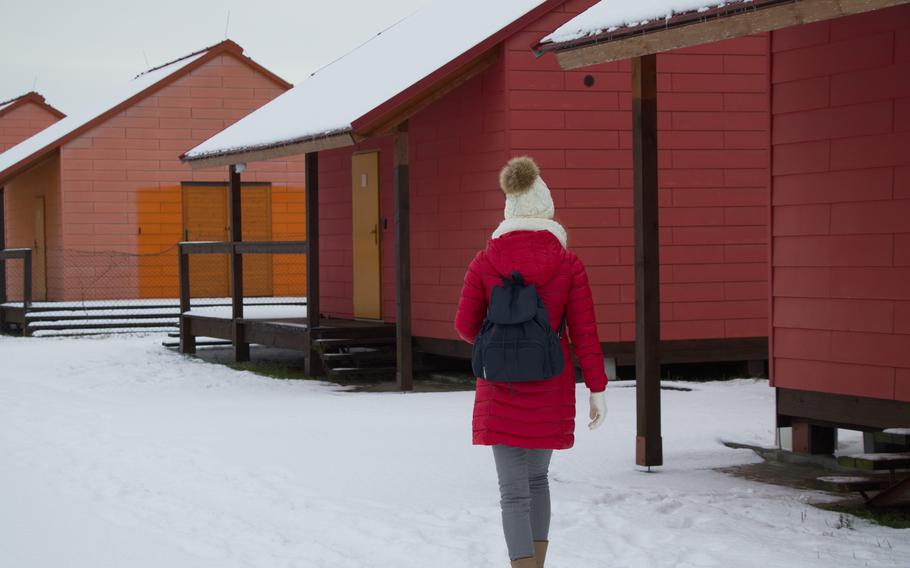 Woman with a red puffy coat walking on a snow covered road past 3 red camping cabins