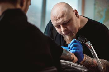 Male tattoo artist tattooing another man’s arm.