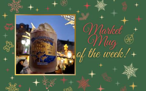 Photo Of An up-close photo of a frosted market mug with blue and gold detailing of the city and lillies, filled with hot chocolate and whipped-cream. 