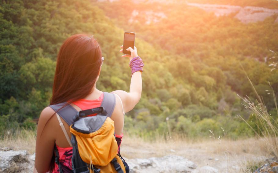 Young woman hiker taking selfie with mobile phone in mountains at sunset