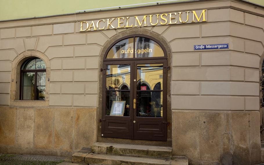 A tan brick building with the gold lettering “Dackel Museum” above arched, glass doors.