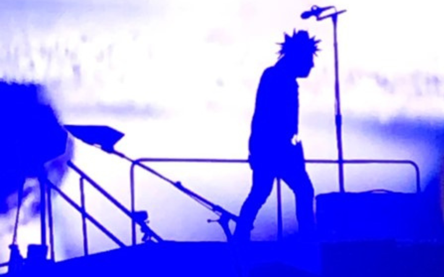 Tool lead singer, standing profile, facing right, standing on stage illuminated in blue and white light