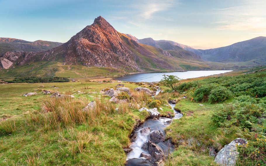 a river lead to a pond and mountain that is reflecting the sunset