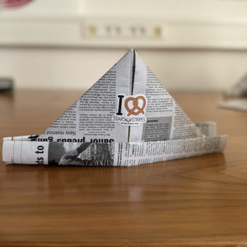 Newspaper hat placed on a table with a Stars and Stripes sticker on the front.
