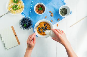 Top view female hands adding milk to cereals bowl with berries. 