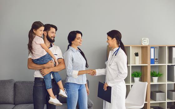 Young happy family with small daughter saying goodbye to woman doctor and shaking hands after successful visit in medical clinic office. 