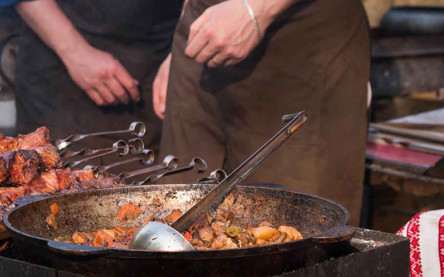 ratatouille in a old cauldron and ladle, barbecue, chef`s hands on background