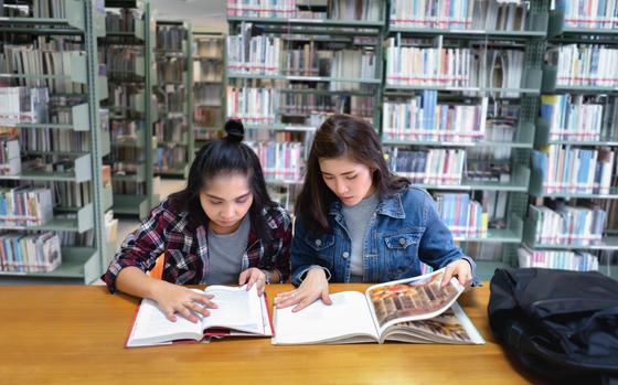 Photo Of Two female students open reading a textbook in the library room.