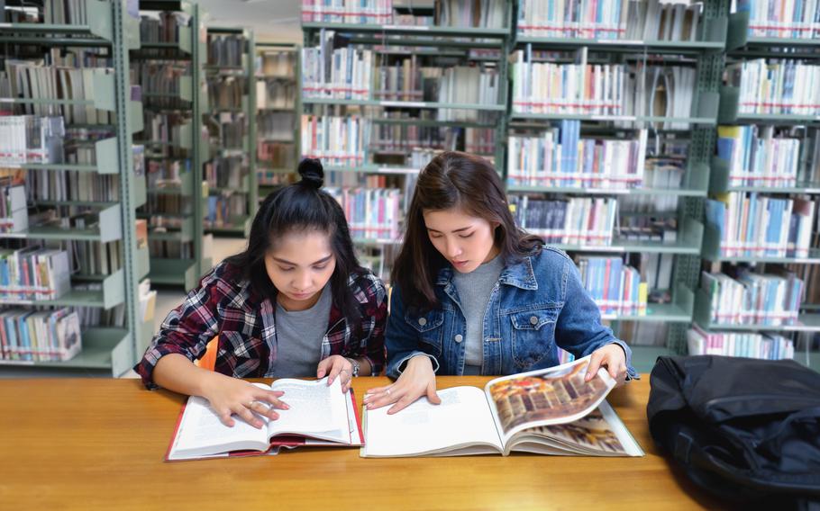 Two female students open reading a textbook in the library room.