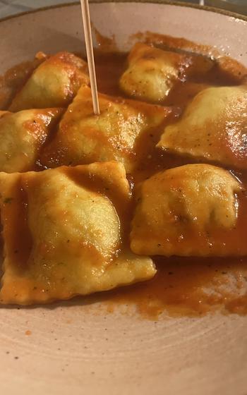 A plate of square raviolis coated in tomato sauce
