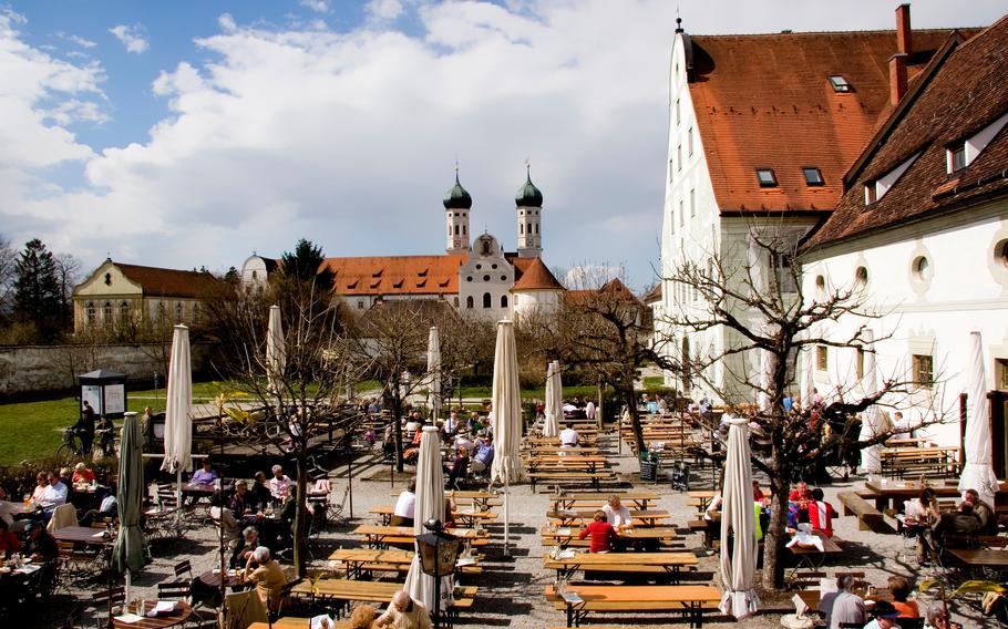 A beer garden on the sunny grounds of a monastery with two towers.