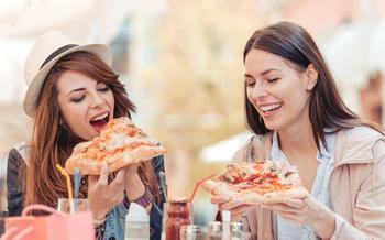 Two cheerful girls eating pizza in a outdoor cafe,relaxing after shopping.