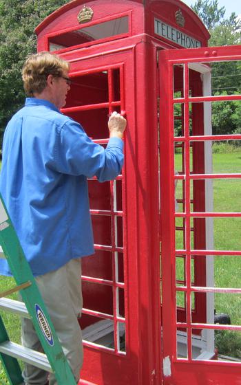 Man standing on green ladder painting the phonebooth red
