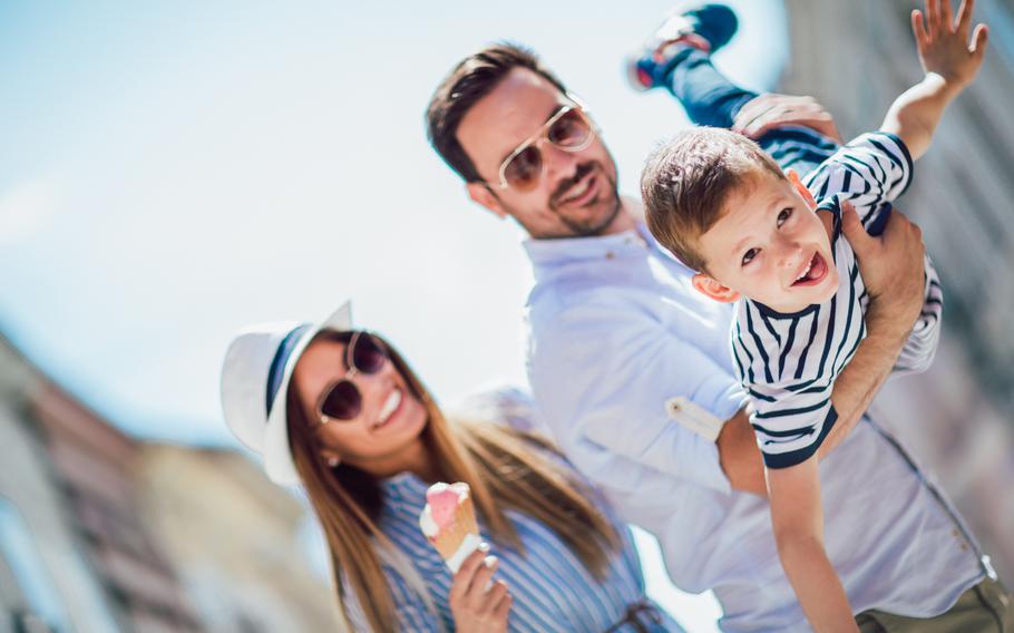 Women is holding ice cream cone and looking at man holding a young boy who has his arms stretched out as if he is flying like a plane