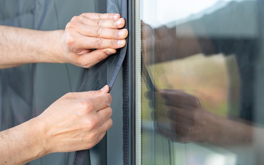 hands are applying a insect screen to a window