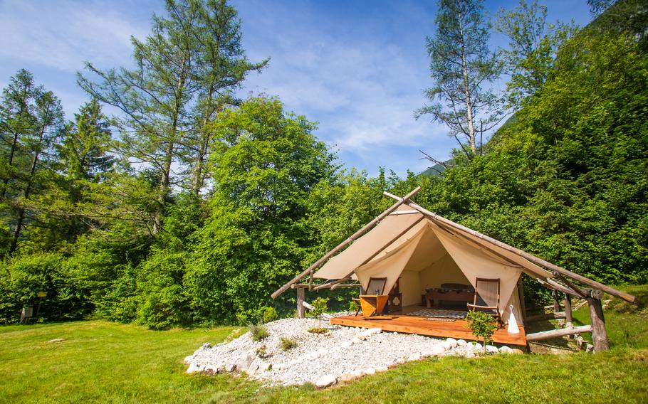 a green field with a tent set up on white rocks with lounge chairs. 