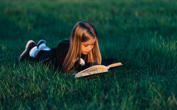 A child lies on the grass and reads a book in the sunset light.