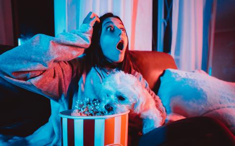 Photo Of Close up portrait of young girl at home in a dark room with a popcorn bucket playing with her dog and sits in front of a monitor or TV.