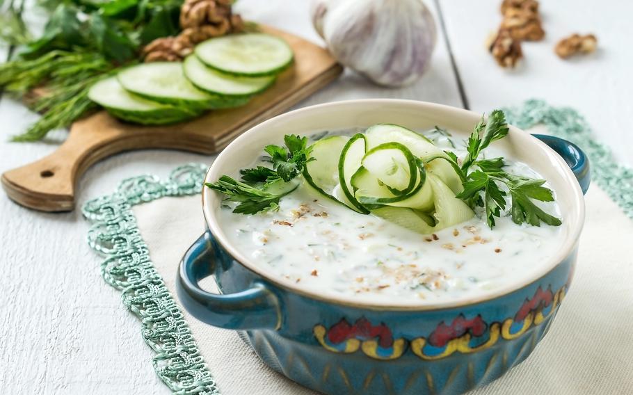 a cold white soup n a blue bowl adorned with cucumbers