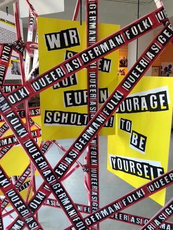 Warning tape in Gay Museum. The tape reads (in English) “Queer as German Folk”