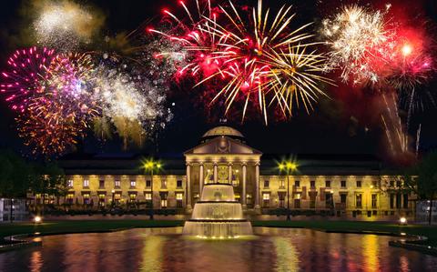 Photo Of Bright red and gold fireworks light the sky above a lit-up building